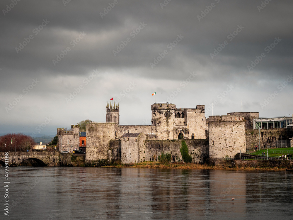 King Jonh's castle on River Shannon, Limerick city, Ireland. Popular museum and landmark. Fine example of stone stronghold with tall walls and towers. Cloudy sky. Building reflection in water.