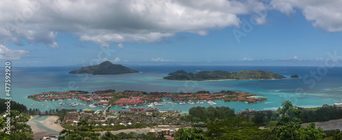 A high-resolution panoramic photo of a tropical island coastline. This is view from La Misere View Point on Mahe island in the Seychelles. Panorama filled with ocean, rainforest and bungalow hotels. 