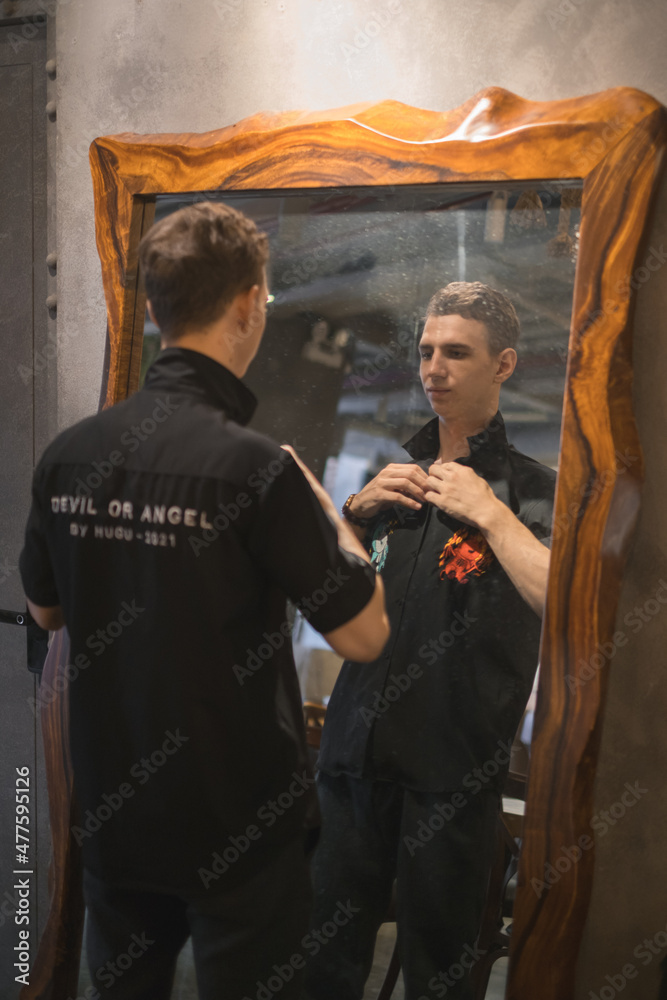 Portrait of young caucasian man in black polo standing in cafe and looking at the mirror. High quality photo