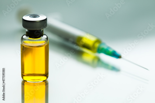Yellow liquid in glass ampoule vial next to syringe with needle