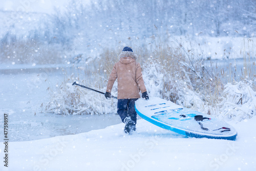 Winter SUP. Man goes to the river to ride a supboard in the snow