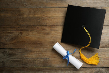 Graduation hat and diploma on wooden table, flat lay. Space for text