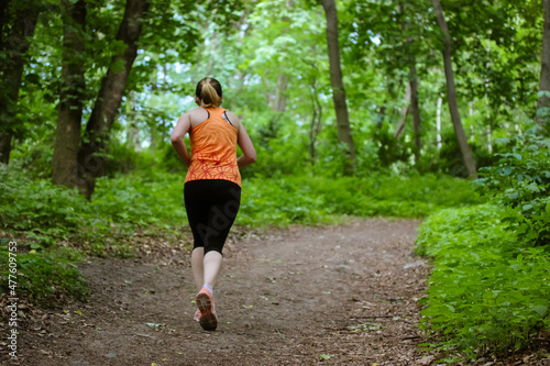 Jogger in green woods. Woman running on dirty road in forest. Hiker girl in athletic shorts, sneakers sportswear jogging outdoors in park in spring, summer day. Jogging In nature. Resuming a workout.