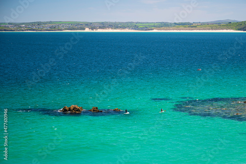 Two paddleboarders, in the clear blue sea off the coast of St. Ives, Cornwall, England, on a clear summer's day