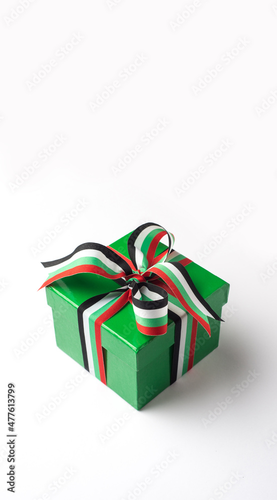 A paper gift box wrapped with UAE flag color ribbon shot on white background. UAE national day celebration elements and objects. A paper gift box wrapped with UAE flag color ribbon shot on white background. UAE national day celebration elements and objects.
