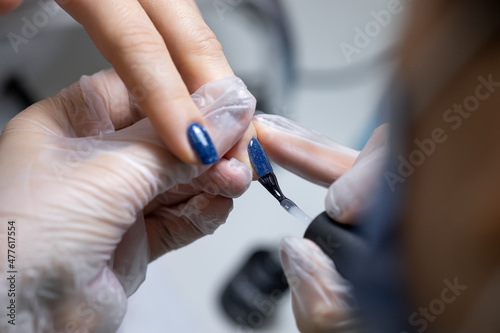 the manicure master holds the client s finger and applies a blue gel polish to the nail