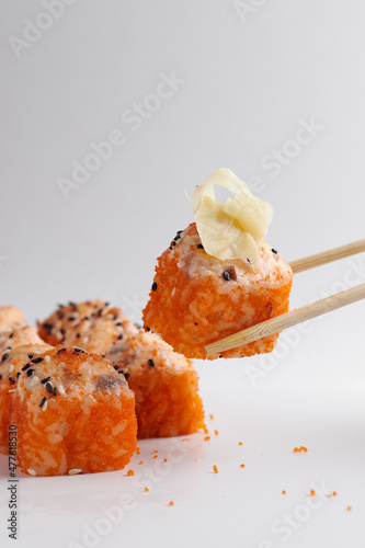 a hand and Chinese chopsticks holds a roll over other sushi, a portion of Asian food, rolls