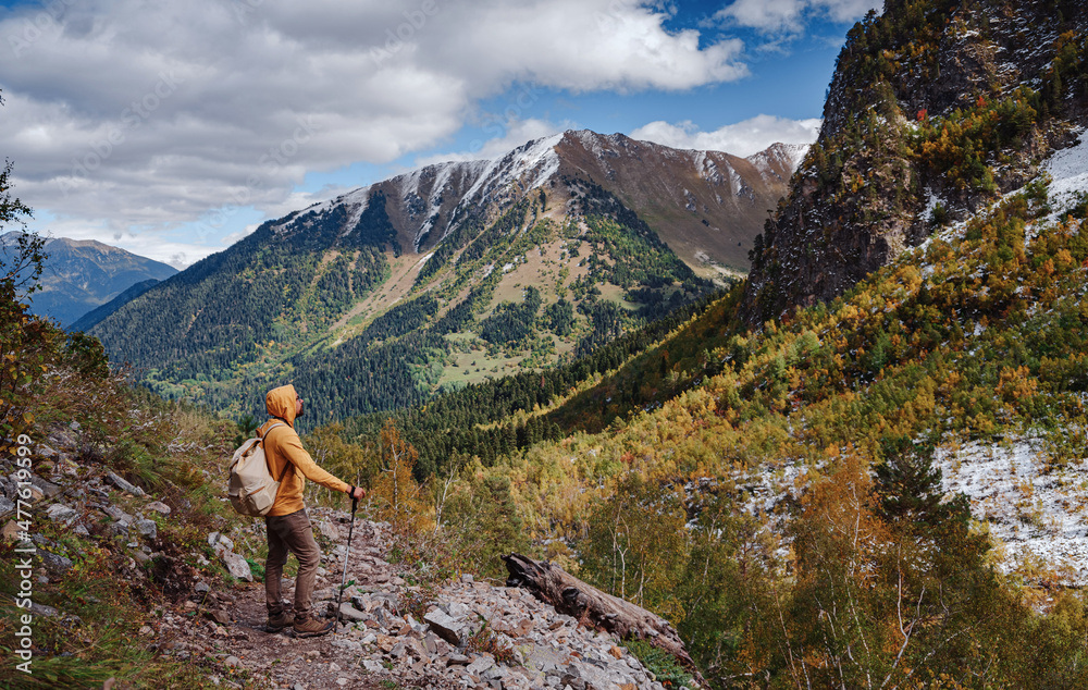 travel to Caucasus mountains in Karachay-Cherkessia, Arkhyz. Man in yellow hipster hoodie hiking in mountains with travel backpack. Wandering lifestyle, adventure concept autumn vacation in wild