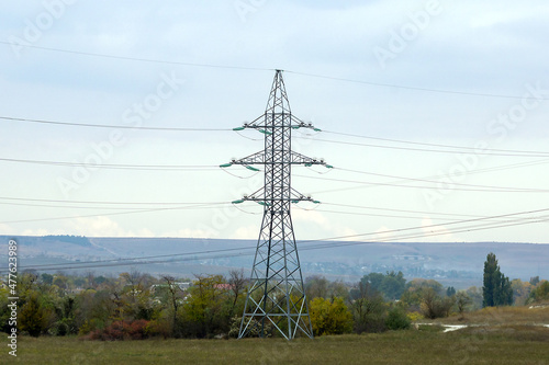 The power line support stands high in the mountains. Photographed in close-up. Electrical wires are connected to the support on both sides.