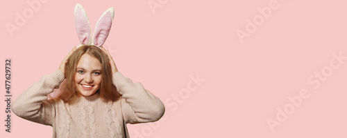 Young blonde smiling sexy woman with bunny ears on a pastel pink background. Easter concept, surprise, emotional Copy space.