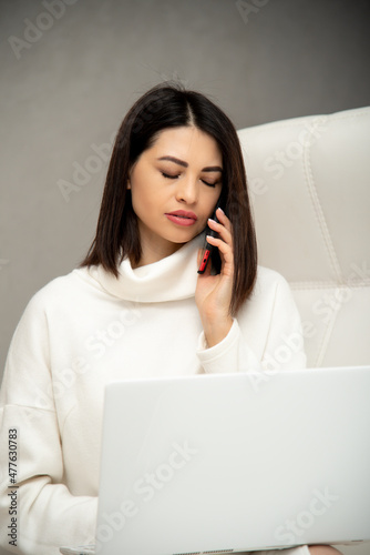 A beautiful young girl sits on a white sofa and works at a computer. Work online. Communication.