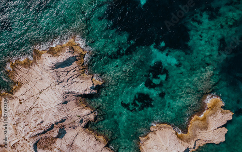 Vertical aerial drone view of the rocky coast and the clear sea of Frioul islands, on a sunny day.