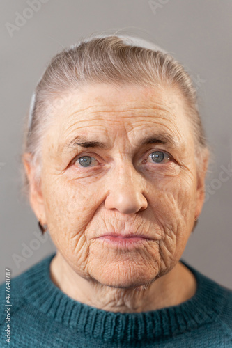 The face of an elderly woman of the 80s with deep wrinkles. Looks at the camera. Portrait of an old lady with gray hair in a knitted green jacket.