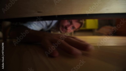 A blond-haired man glancing under the bed on his knees looking for lost socks 