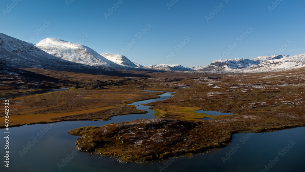 Valley with lake surrounded by snowy peaks at sunny day with no clouds. Scandinavian autumn landscape. Kungsleden trail, Sweden