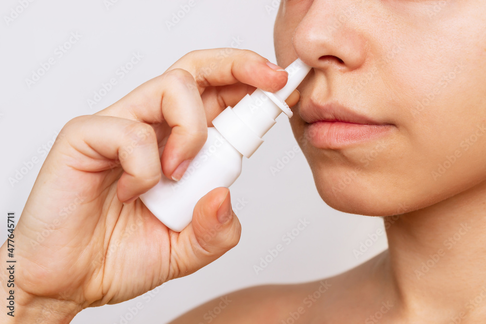 Cropped shot of a young caucasian woman using nasal spray for a runny nose and congestion isolated on a white background. Treatment of the disease. Rhinitis, sinusitis, cold. Dependence on drops - obrazy, fototapety, plakaty 