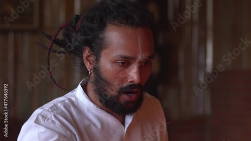 Close-up of young indian man leads Fire ceremony Agni hotra, Hindu rituals, Yagya. He pours Ghee oil into the fire, sings mantras. Slow motion.