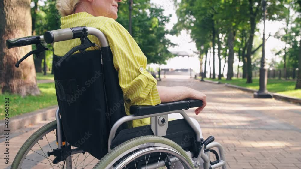 Senior retired woman with physical disability relaxing in park, wheelchair user Senior retired woman with physical disability relaxing in park, wheelchair user
