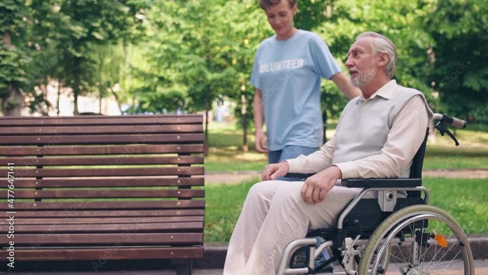 Happy volunteer assisting retired man in wheelchair, professional assistance Happy volunteer assisting retired man in wheelchair, professional assistance