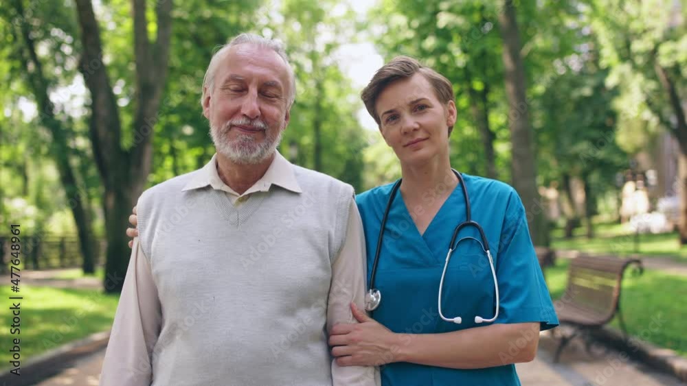 Nurse with stethoscope hugging smiling aged man, working in nursing home, care