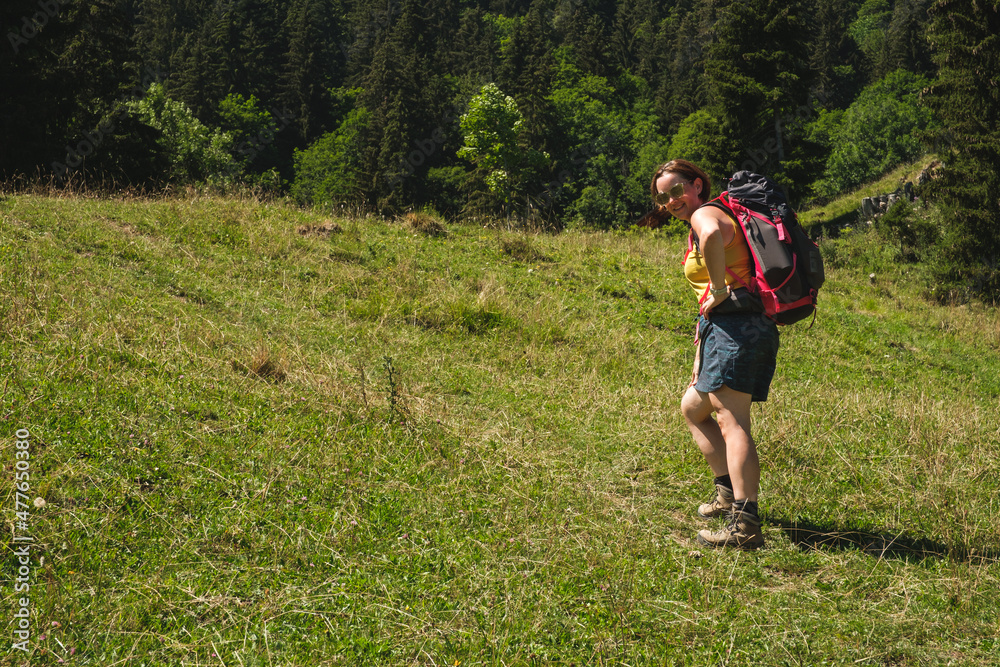 Attractive woman hiking with backpack wearing sunglasses on sunny day in summer looking down to camera Attractive woman hiking with backpack wearing sunglasses on sunny day in summer looking down to camera