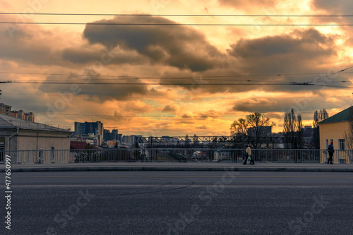 An empty road and several pedestrians are walking at dawn. On the bridge over the railroad tracks