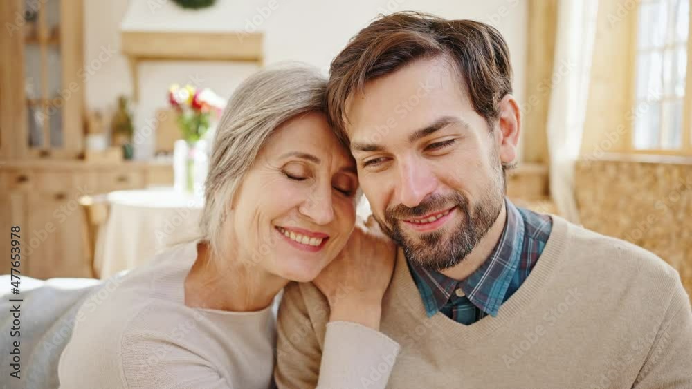 Close up portrait of young loving son cuddling together with his beautiful senior mother, enjoying happy time together