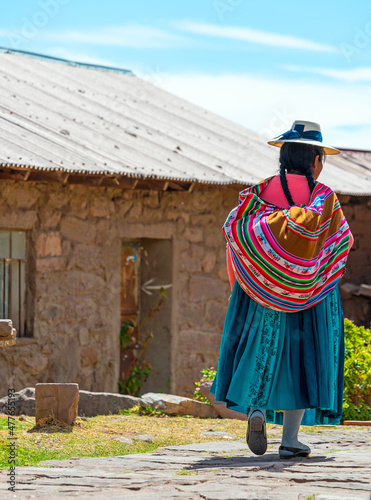 Unrecognizable indigenous Peruvian Quechua woman in traditional clothing walking in a street of Taquile Island by the Titicaca Lake, Peru.