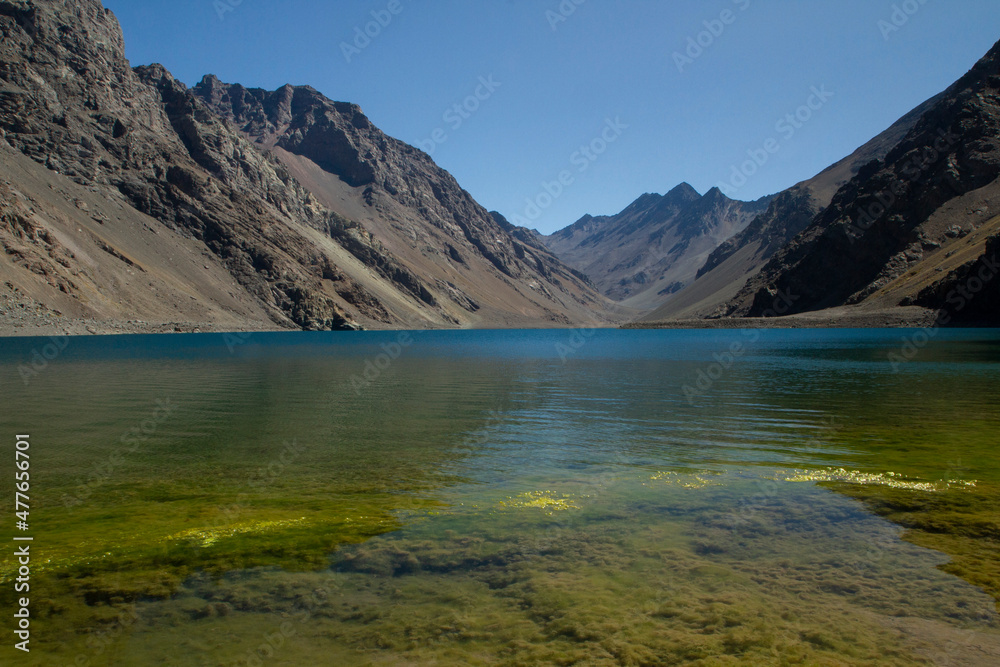 The colorful lake called Inca Lagoon in the Andes mountain range. The blue glacier water and yellow shallows surrounded by rocky mountains.