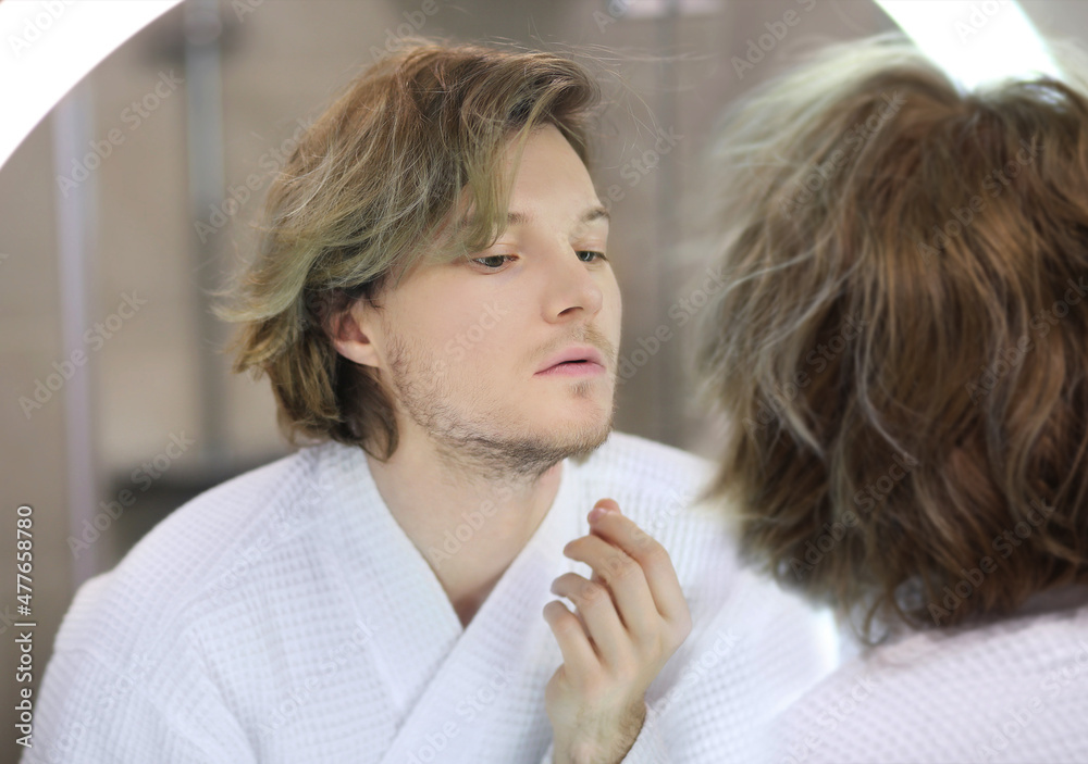 young man looking in the mirror,combing his hair,looking at problems on face. young man looking in the mirror,combing his hair,looking at problems on face.