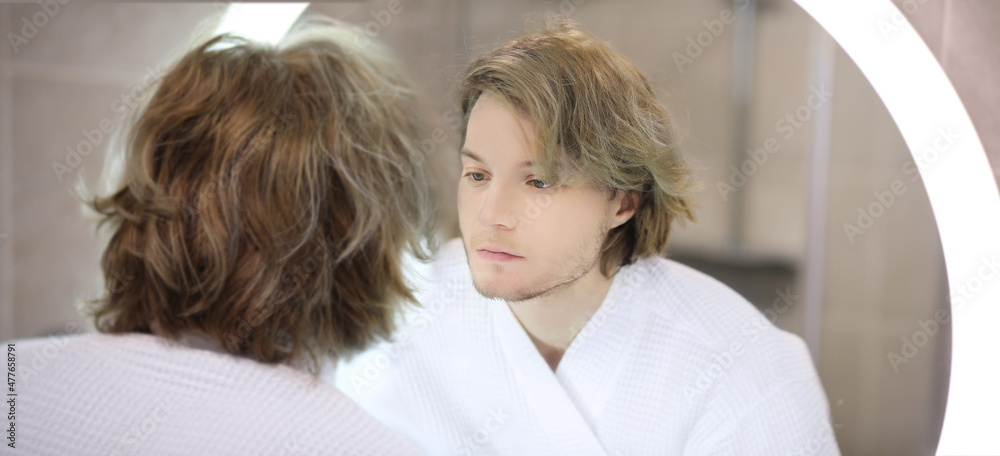 young man looking in the mirror,combing his hair,looking at problems on face. young man looking in the mirror,combing his hair,looking at problems on face.