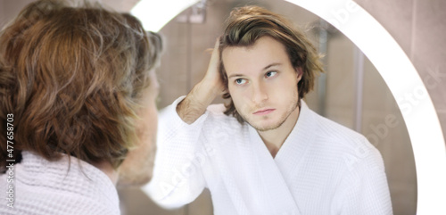 young man looking in the mirror,combing his hair,looking at problems on face.