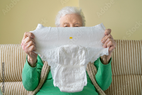 wrinkled hands of a senior woman or man holding white adult diaper pad
