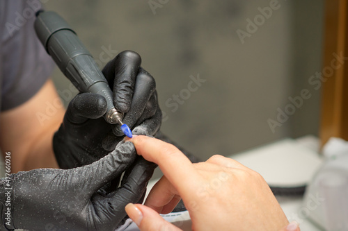 Manicurist removes nail polish uses the electric machine of the nail file during manicure in a nail salon photo