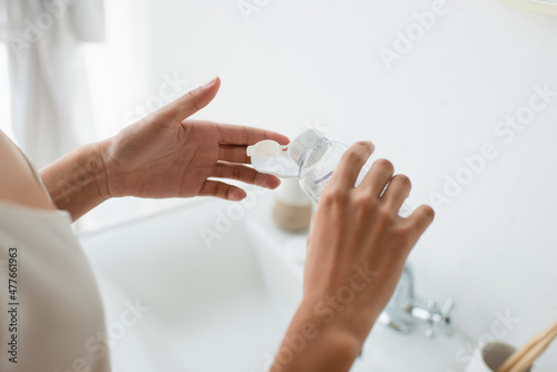 Cropped view of african american woman pouring lotion on cotton pad in bathroom.
