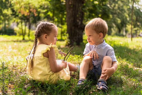 Two happy smiling cheerful toddler preschool twins siblings children brother sister boy girl communicate talk together on grass lawn in park in sunny hot summer. childhood, friendship, family concept