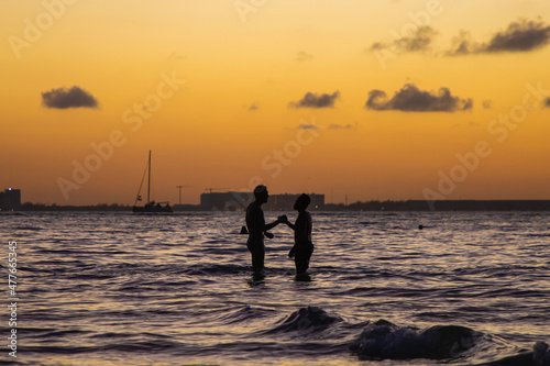 Dos amigos saludándose afectivamente durante el atardecer en playa norte en Isla Mujeres, 