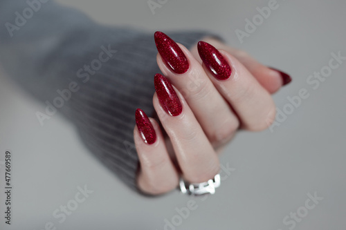 Murais de parede Female hand with long nails and a dark red manicure holds a bottle of nail polis