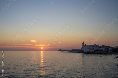 A scenic sunset is reflected in the Mediterranean Sea, with the city of Sitges in the background.