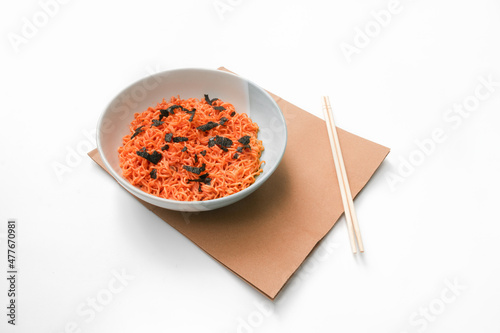 Korean-style instant noodles in a white bowl laid out on brown paper with chopsticks on the side, photographed from the front and against a white background. Used in food and health applications