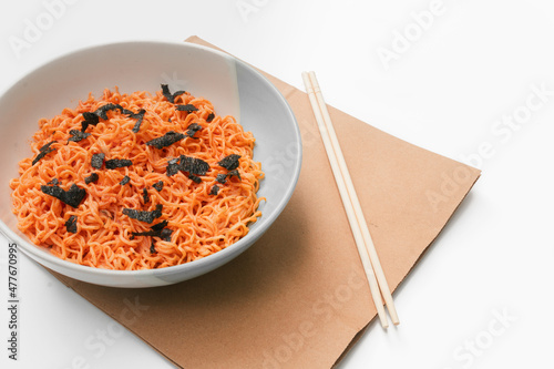 Korean instant noodles menu in a white bowl on brown paper with chopsticks on the side, close-up shot against a white background. Used in food and health applications