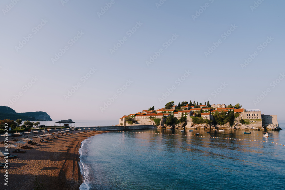 Sandy beach with sun loungers and umbrellas leading to Sveti Stefan Island