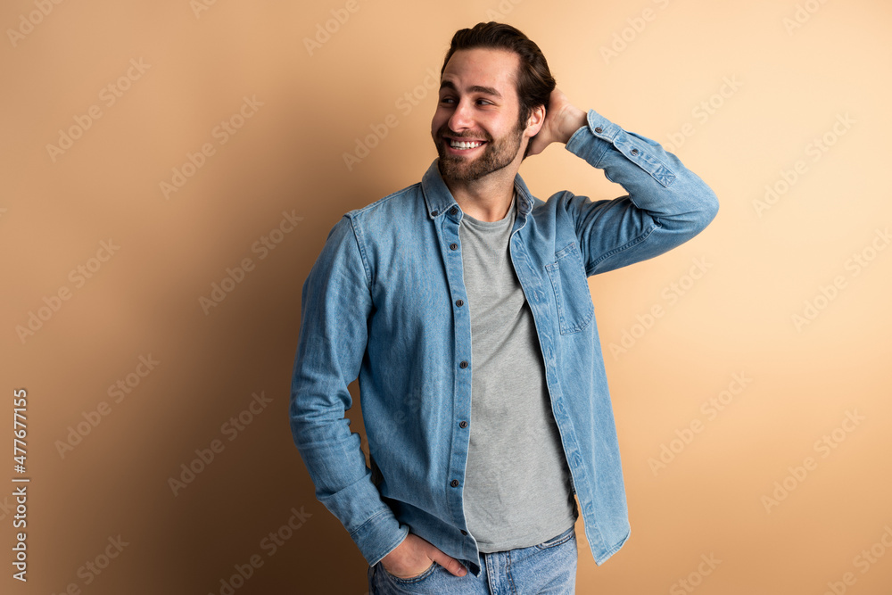 Handsome man with dark hair and beard standing with hand at his head, looking at camera Handsome man with dark hair and beard standing with hand at his head, looking at camera