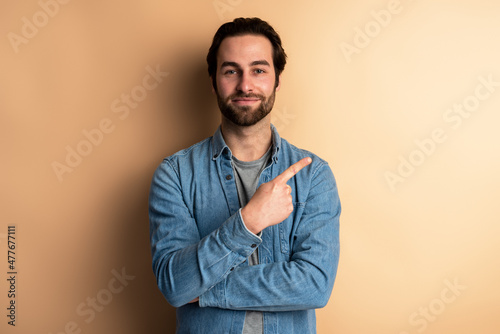 Portrait of positive friendly brunette man with beard standing and pointing at right