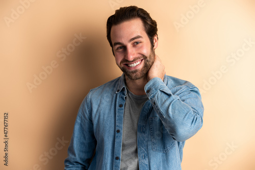 Happy smiley bearded man with dark hair holding his hand at his neck while posing