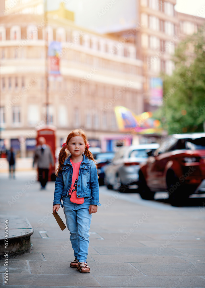 Fototapeta premium a cheerful smiling red-haired girl in a denim jacket walking around the city and having a fun