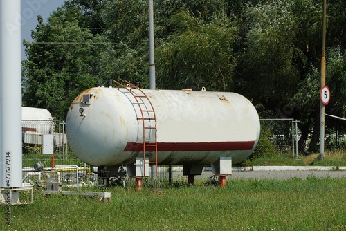 one large industrial iron white barrels with red staircase at a gas station stand on a green grass in the street