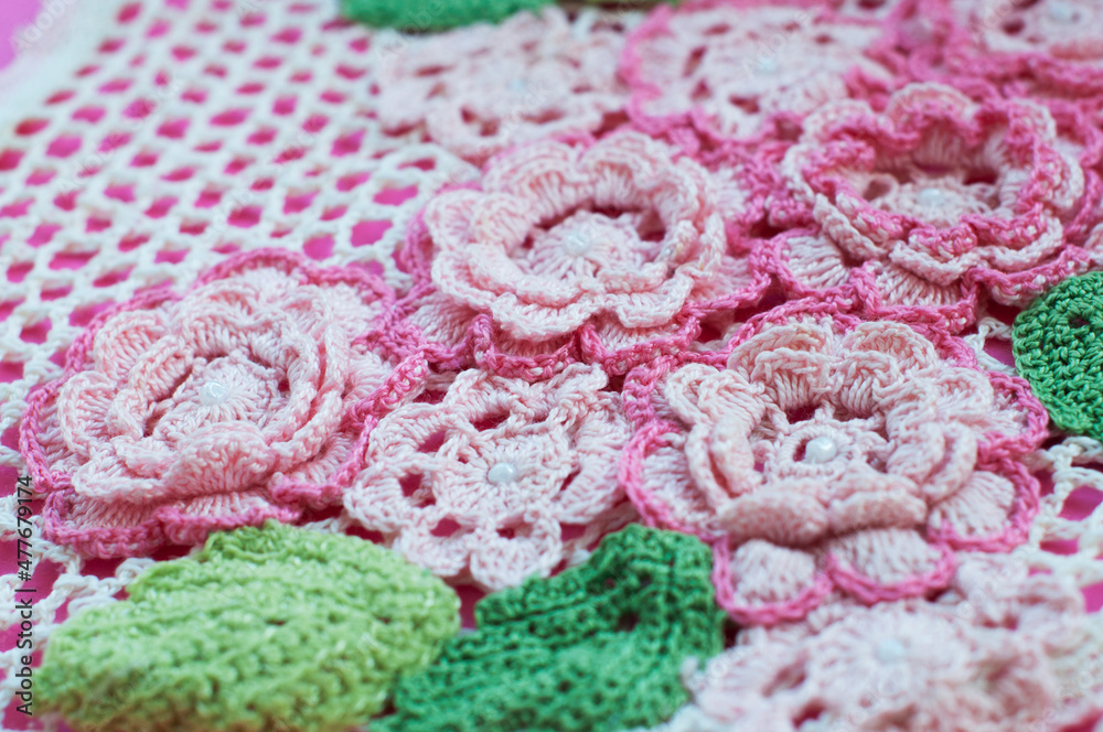 Pink knitted flowers and green knitted leaves on a pink background. Knitted texture Pink knitted flowers and green knitted leaves on a pink background. Knitted texture