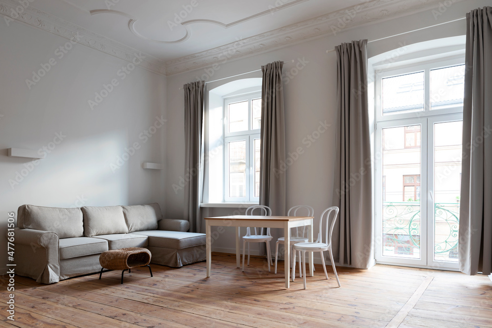 Fototapeta premium Modern living interior with window and comfortable sofa in industrial loft apartment. New living room with dining table and chairs and wooden floor. 