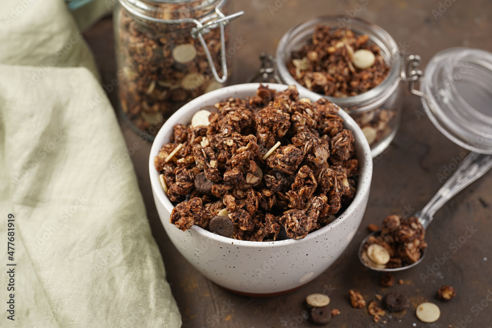 Breakfast muesli cereal with chocolate chips and nuts in several jars and bowl, bottle of milk, brown wooden surface Breakfast muesli cereal with chocolate chips and nuts in several jars and bowl, bottle of milk, brown wooden surface